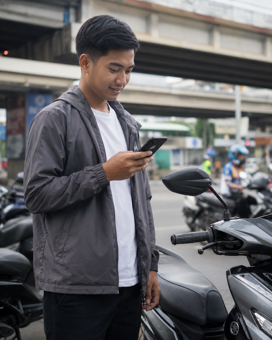 Rider booking a motorcycle on a phone beside a parked scooter